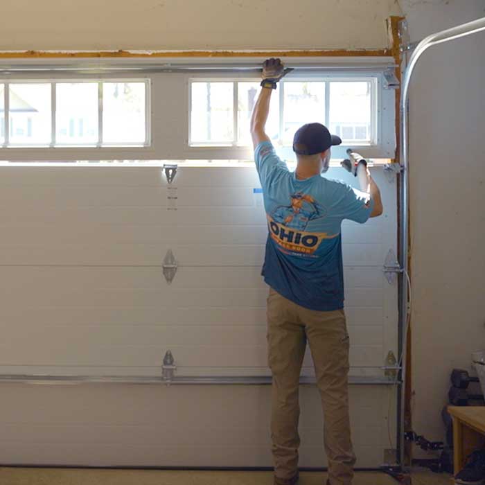 An Ohio Garage Door Repair technician is using a drill to fix a garage door spring near Mentor, OH